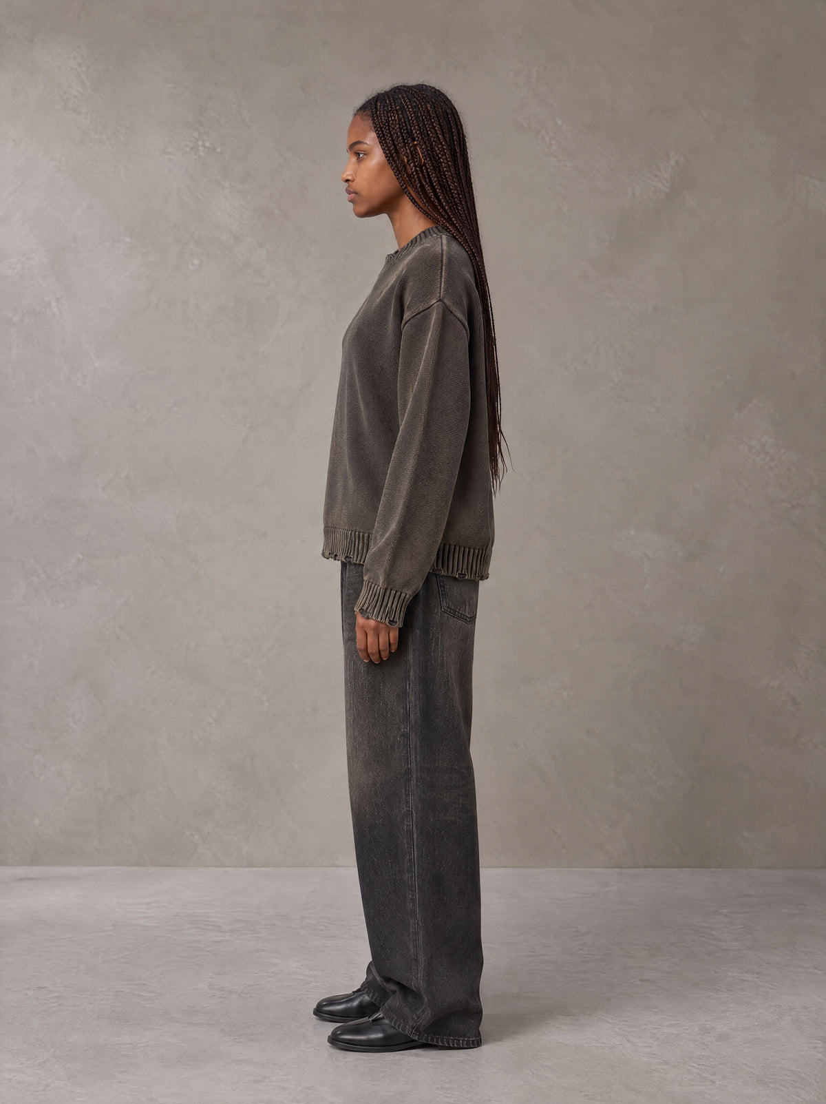 Model wearing the SM Sig. Washed Distress Knit Sweater in Kabul Brown with SM Archive Fade Denim Jeans in black, side profile.