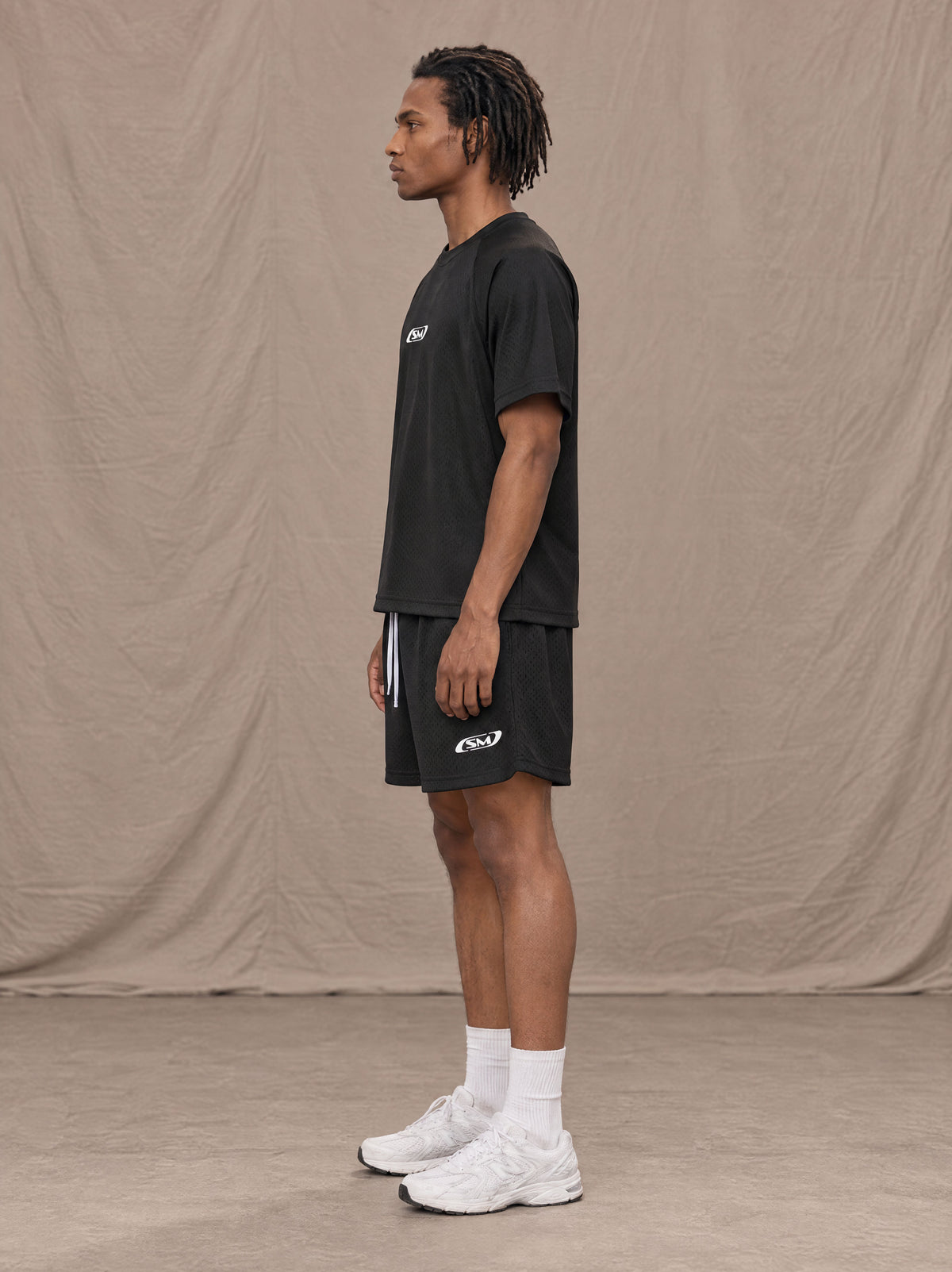 Model wearing the SM Motion Mesh T-shirt and SM Motion Mesh Shorts in black, side profile.