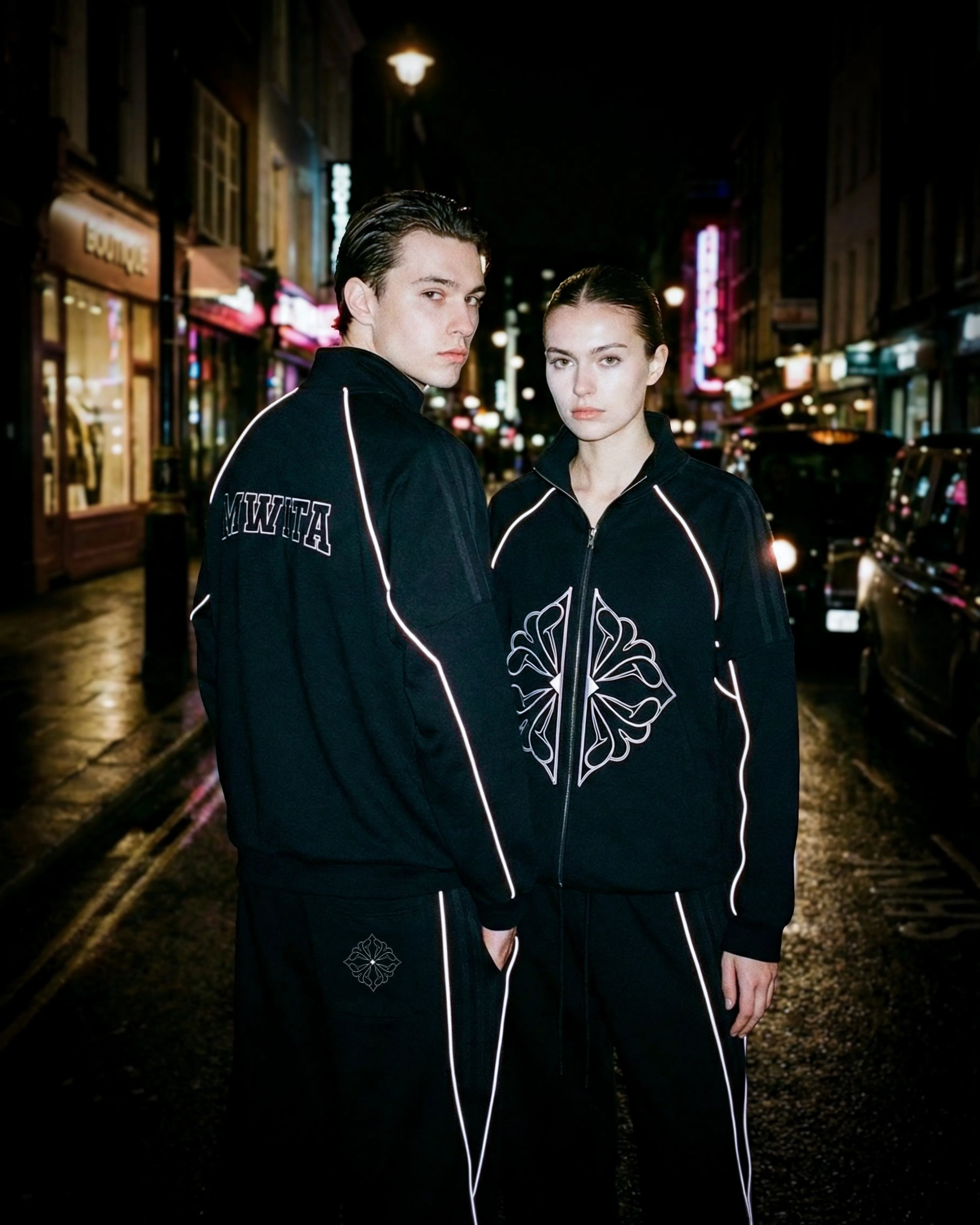 Two models wearing SM Fleur Echo Eclipse Two Piece with reflective piping on a city street at night.