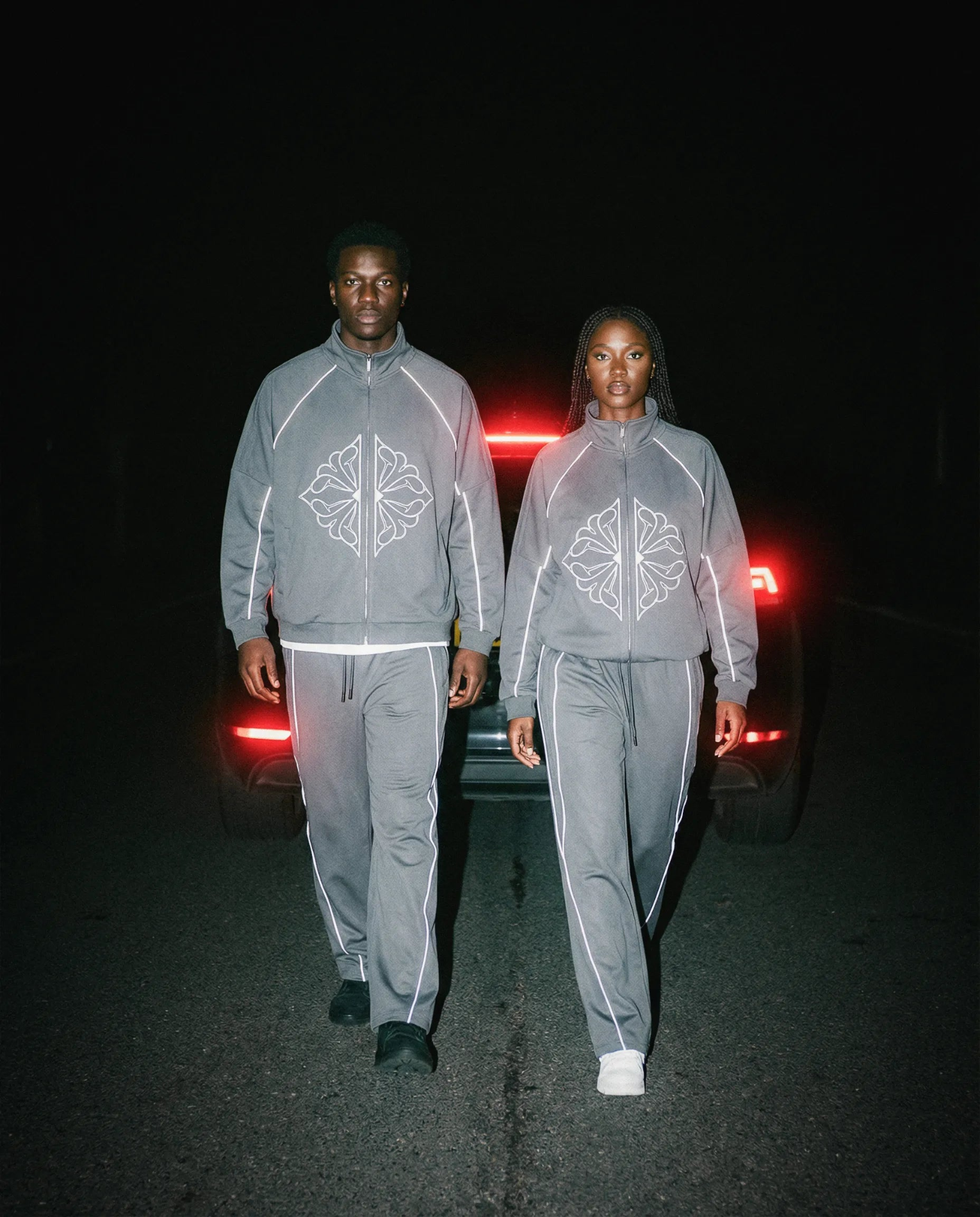 Two models wearing SM Fleur Echo Eclipse Two Piece with reflective piping on a city street at night.