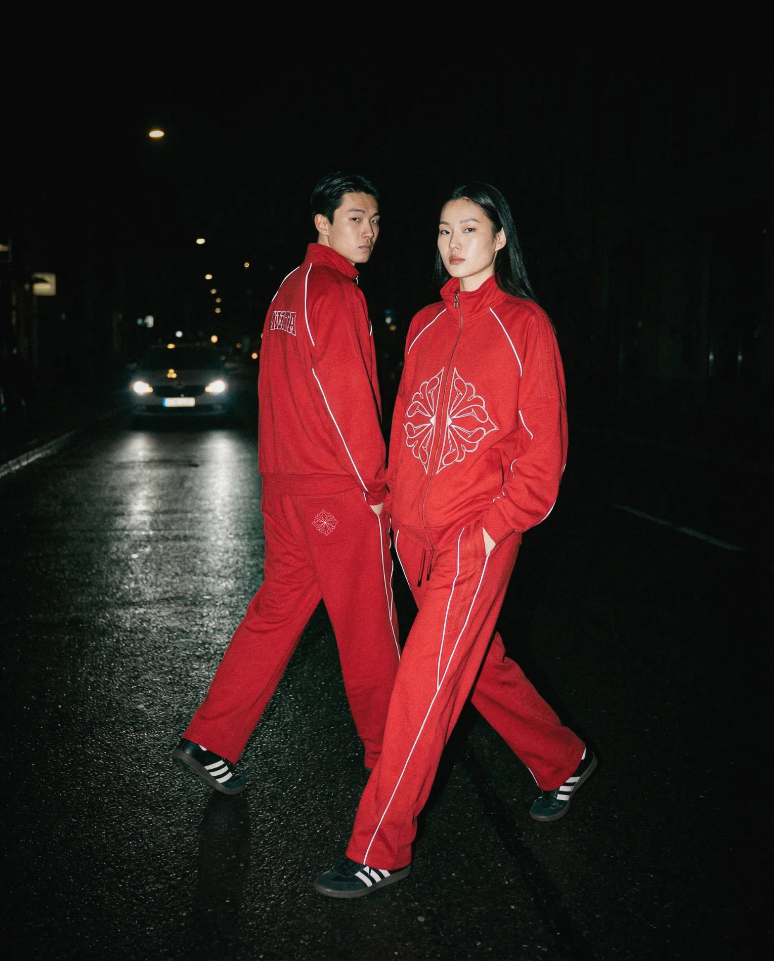 Two models wearing SM Fleur Echo Eclipse Two Piece with reflective piping on a city street at night.