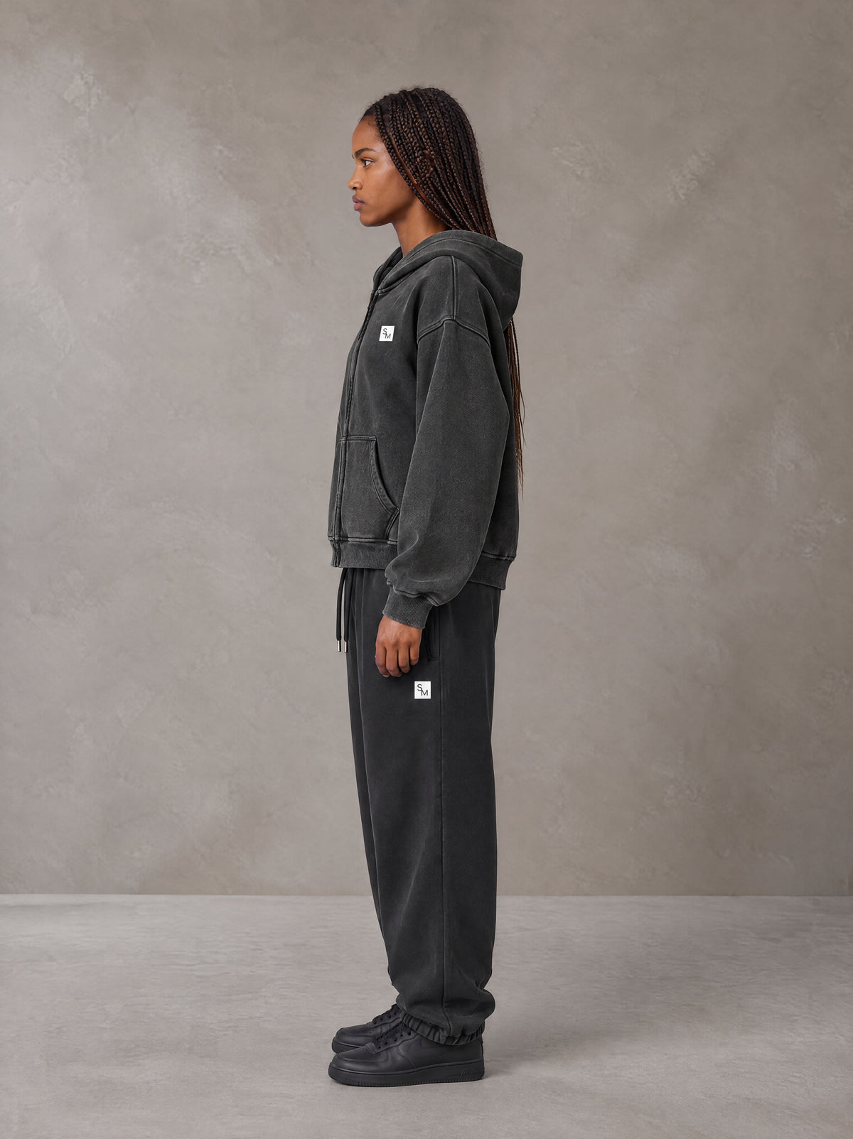 Model wearing the SM Sig. Boxy Hoodie with SM Sig. Jogger Sweatpants in Midnight Black, side profile view.