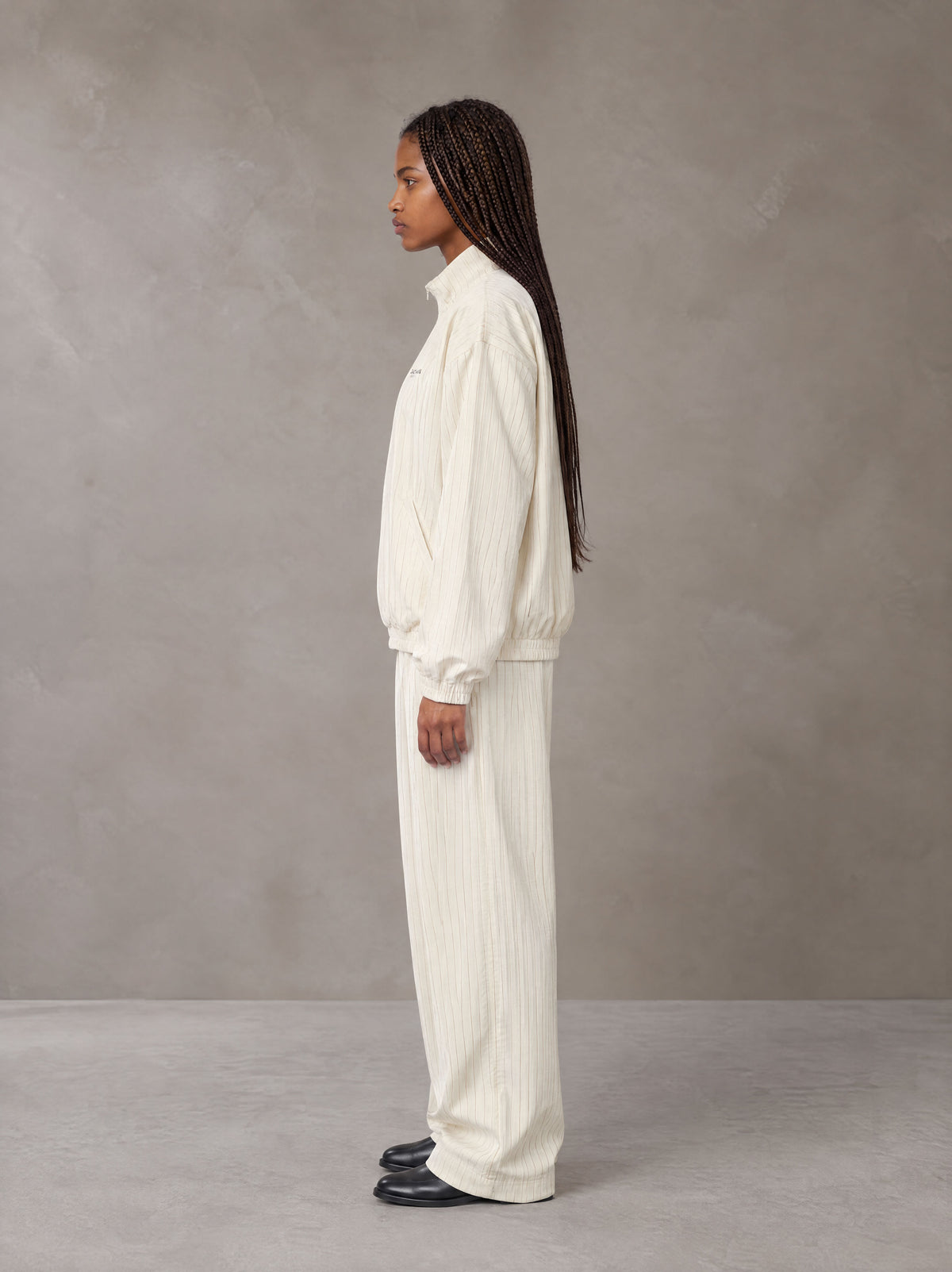 Model wearing the SM Axis Jacket and SM Axis Trousers in Oat Grey, side profile.
