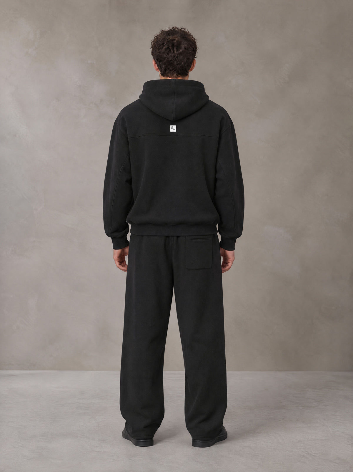Model wearing the SM Shadow Pulse Hoodie and SM Shadow Pulse Sweatpants in Midnight Black, rear view.