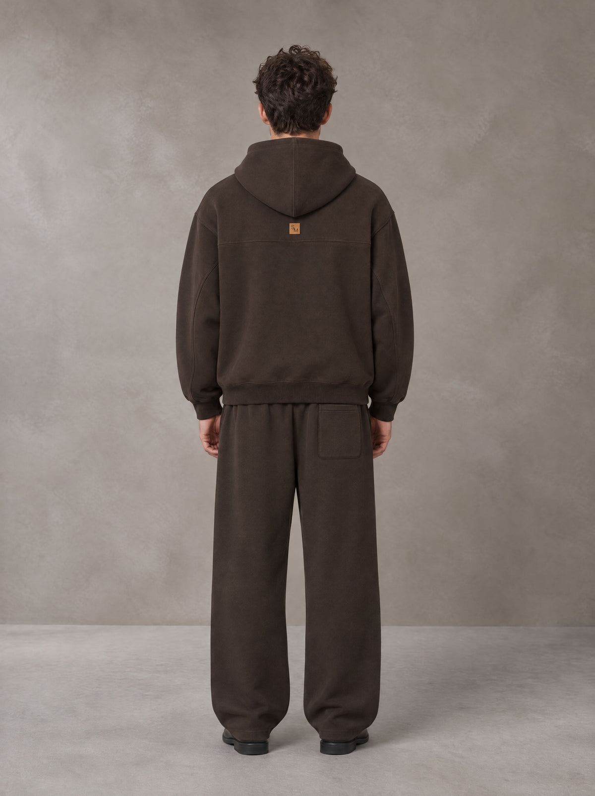 Model wearing the SM Shadow Pulse Hoodie and SM Shadow Pulse Sweatpants in Kabul Brown, rear view.
