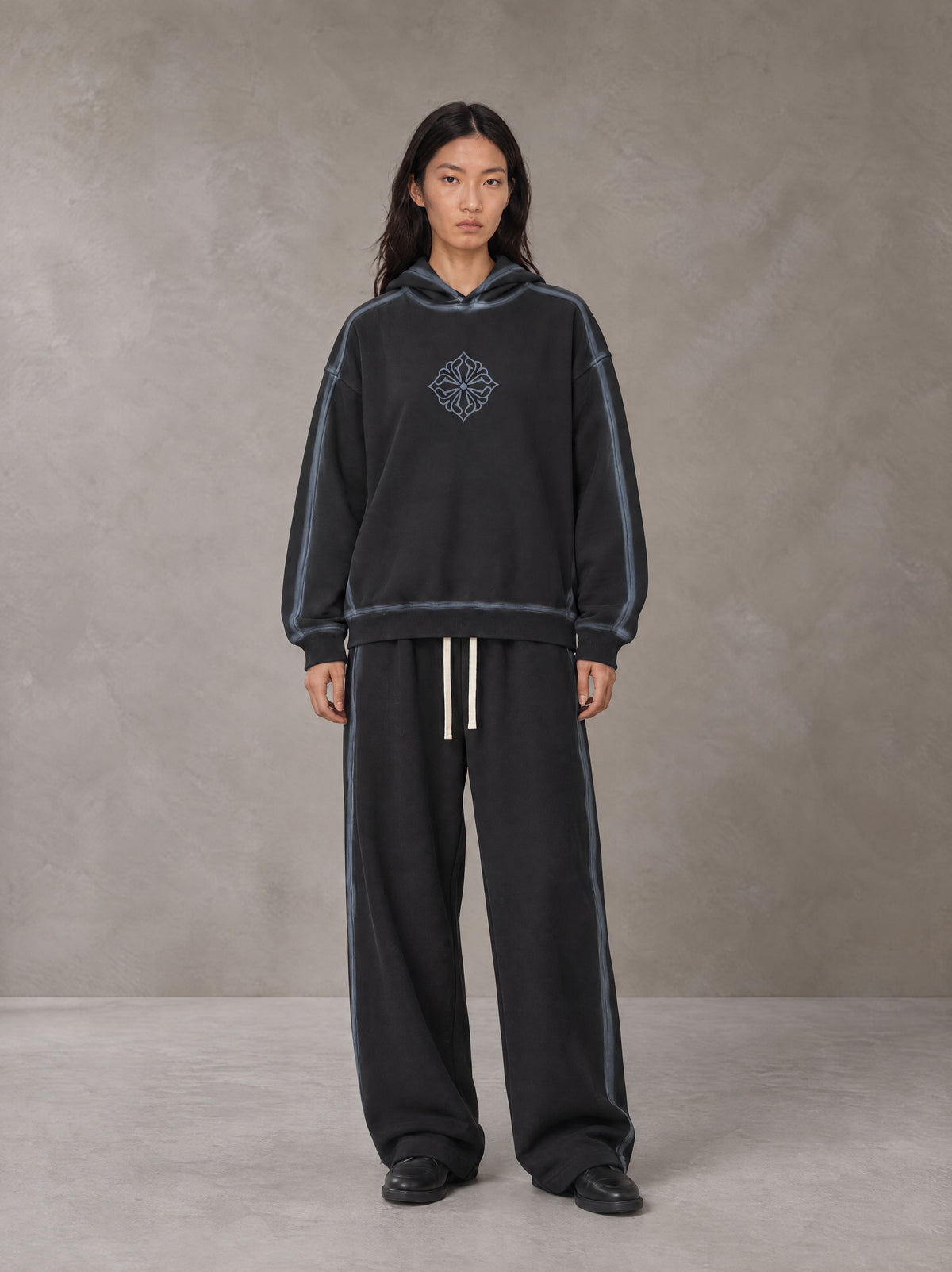Model wearing the SM Grid Fleur Hoodie and SM Grid Fleur Sweatpants in Deep Charcoal, front view.