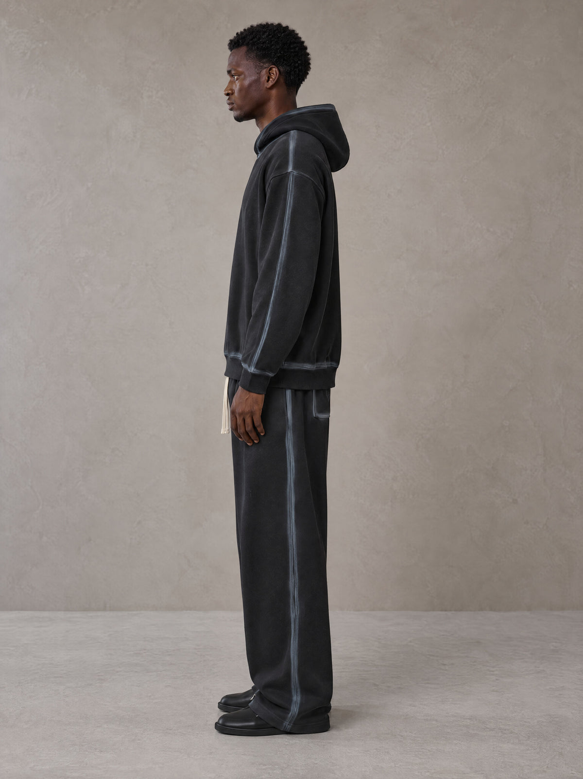 Model wearing the SM Grid Fleur Hoodie and SM Grid Fleur Sweatpants in Deep Charcoal, side profile.