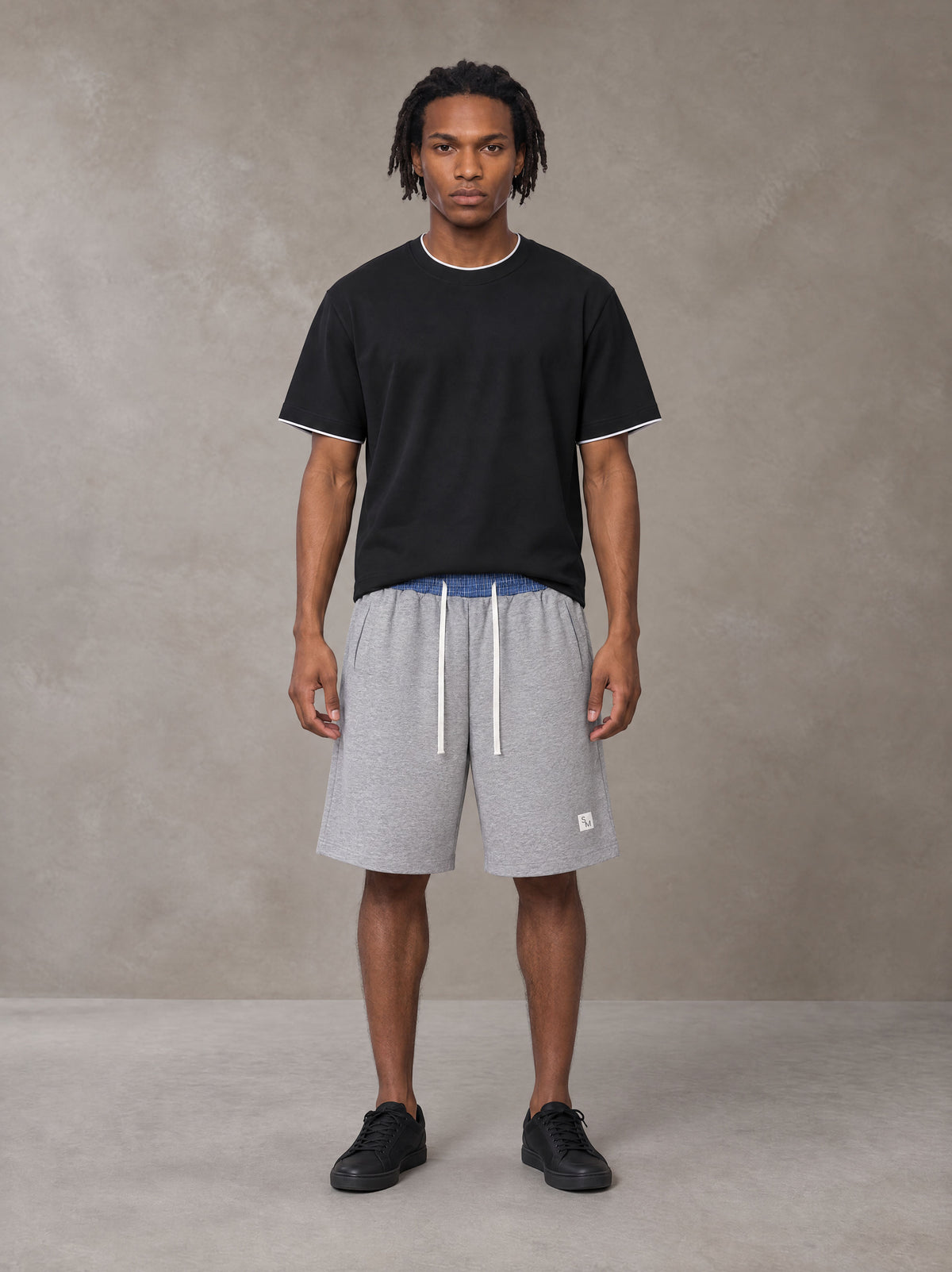 Model wearing SM Plaid Shorts in Floral Grey, front view.