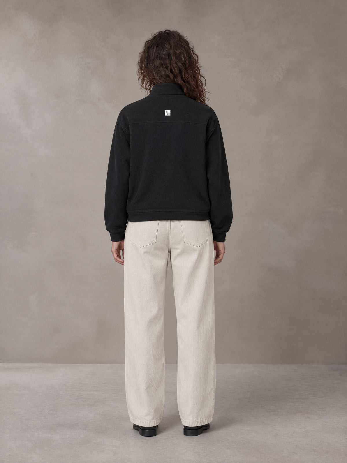 Model wearing SM Sig. Half-Zip Fleece Sweatshirt in Midnight Black, rear view.