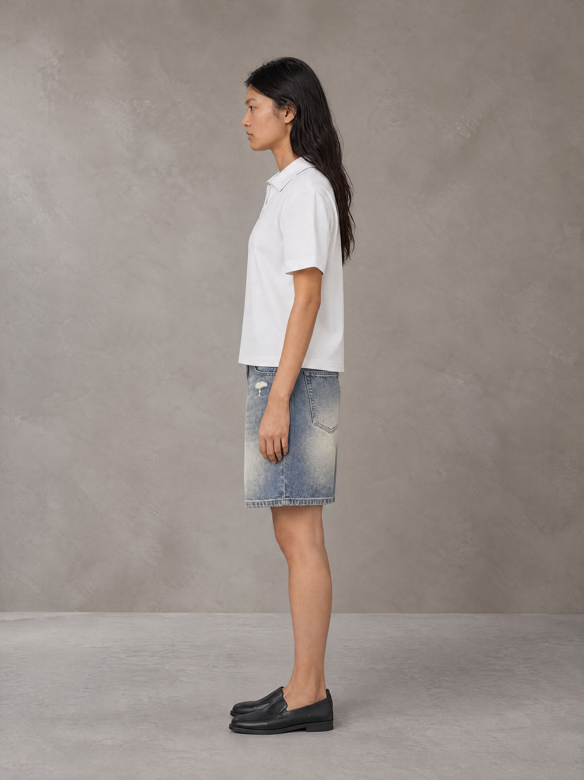 Model wearing SM Heritage Distressed Denim Shorts in Cadet Grey, side view.