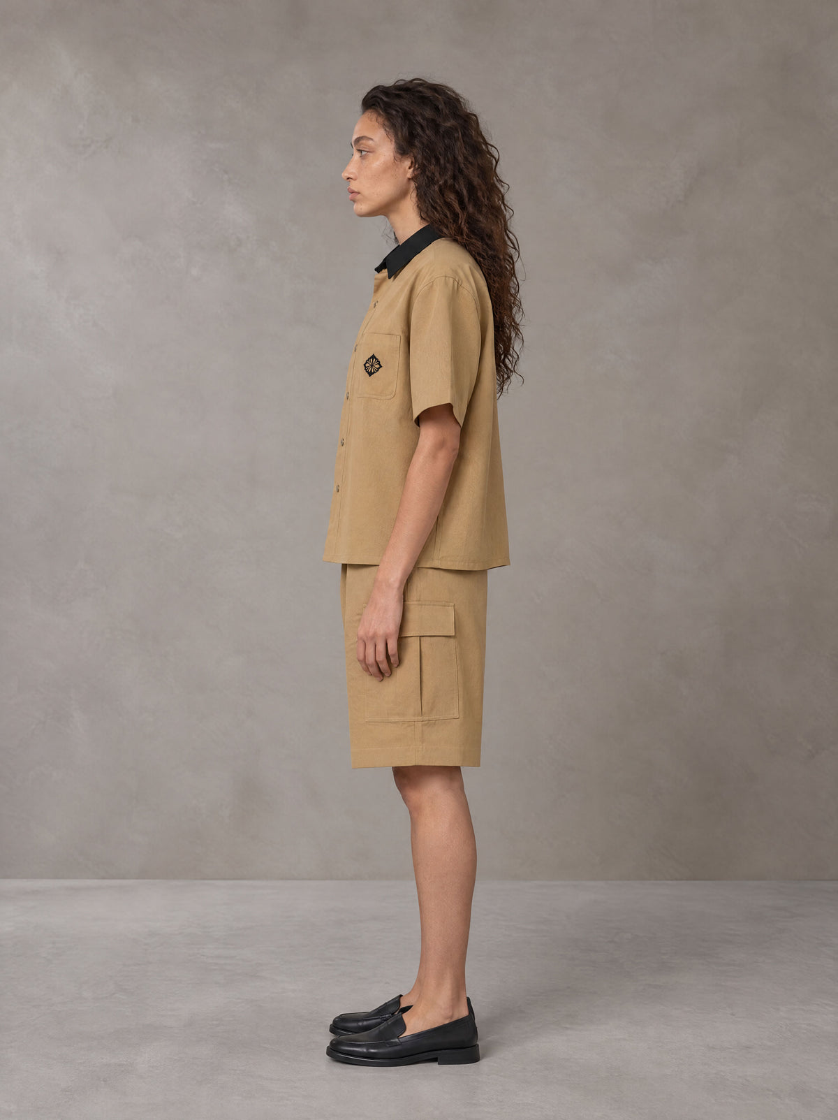 Model wearing SM Eternal Fleur Shirt in Camel Tan with SM Eternal Fleur Utility Shorts in Camel Tan, side view.