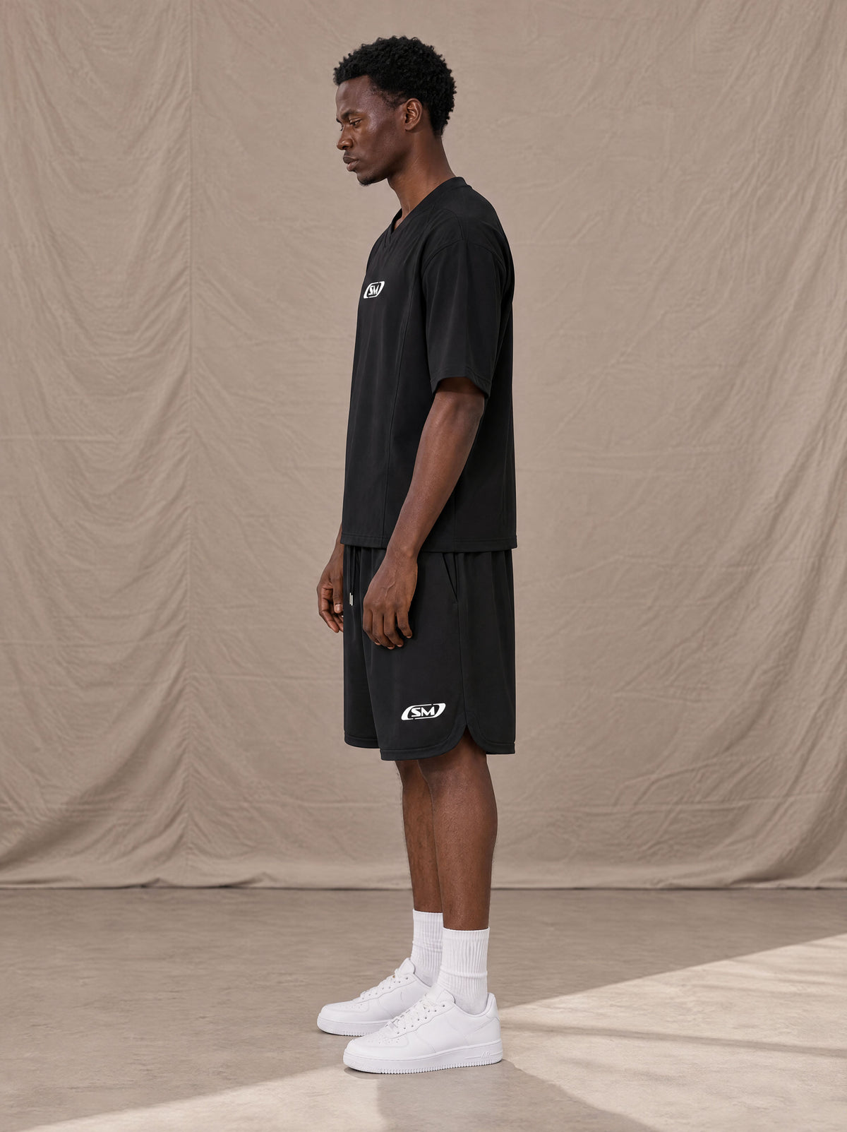 Model wearing SM Motion T-shirt in Midnight Black with SM Motion Oversized Court Shorts in Midnight Black, side view.