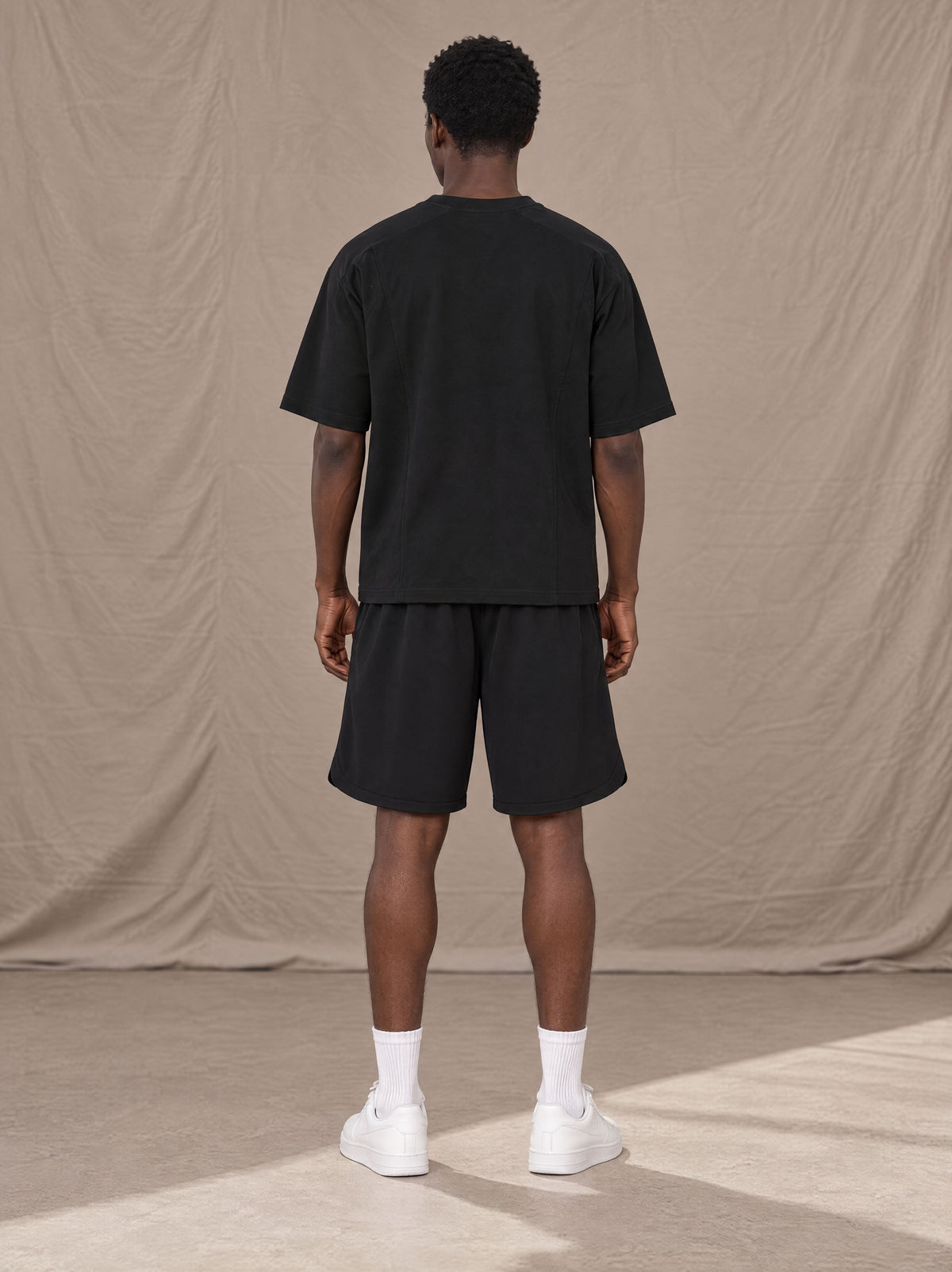 Model wearing SM Motion T-shirt in Midnight Black with SM Motion Oversized Court Shorts in Midnight Black, rear view.