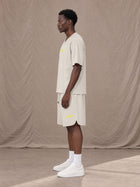 Model wearing SM Motion T-shirt in Oat Grey with SM Motion Oversized Court Shorts in Oat Grey, side view.