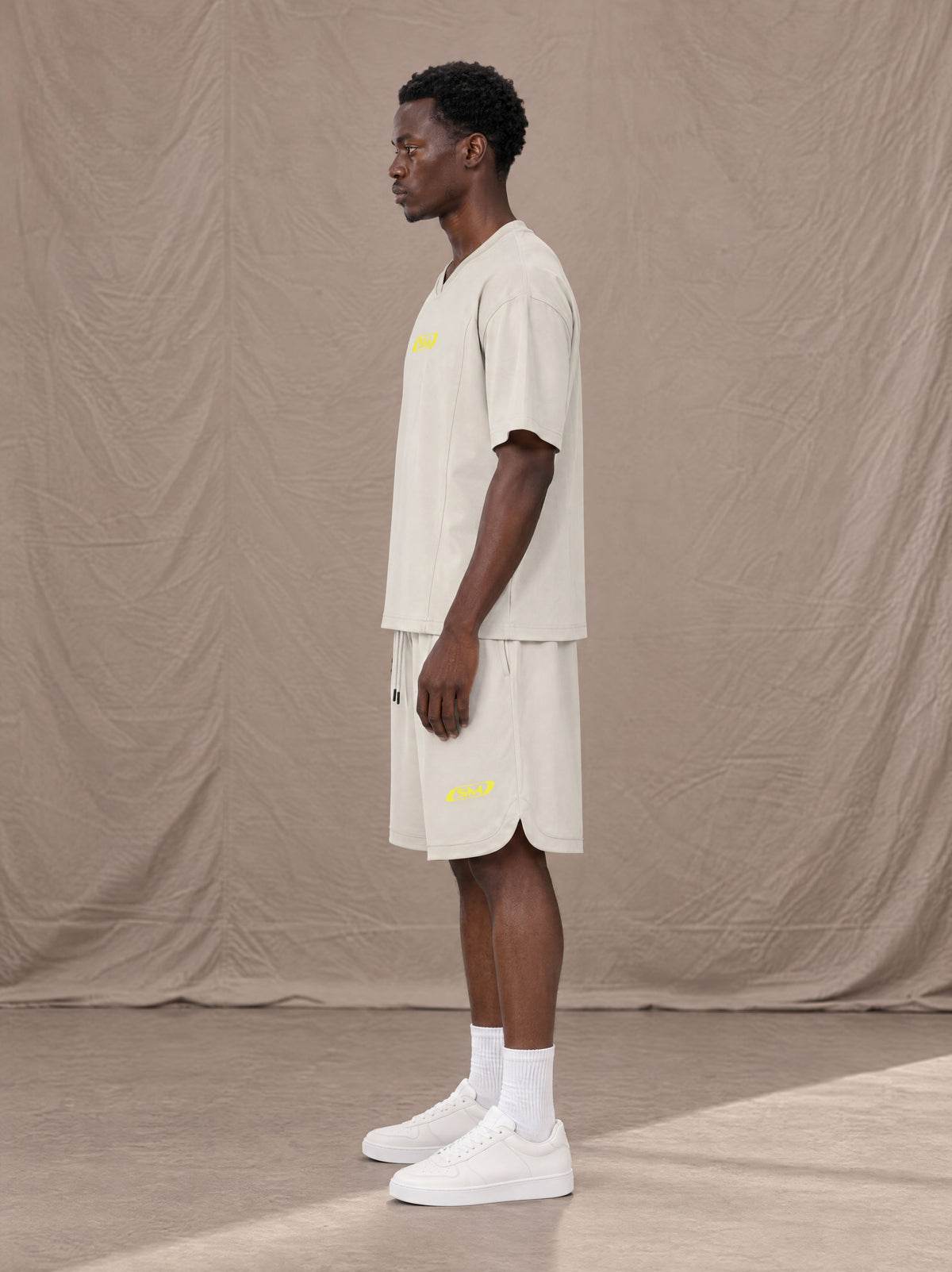 Model wearing SM Motion T-shirt in Oat Grey with SM Motion Oversized Court Shorts in Oat Grey, side view.