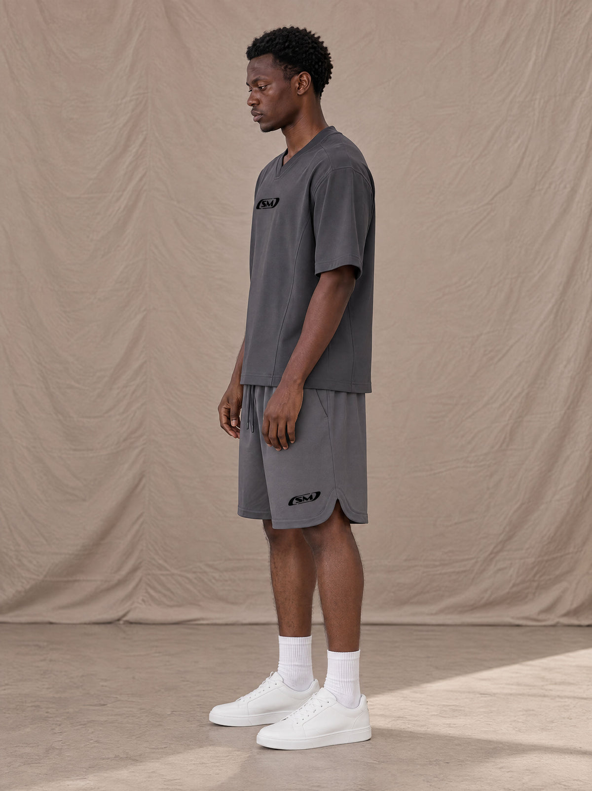 Model wearing SM Motion T-shirt in Deep Charcoal with SM Motion Oversized Court Shorts in Deep Charcoal, side view.