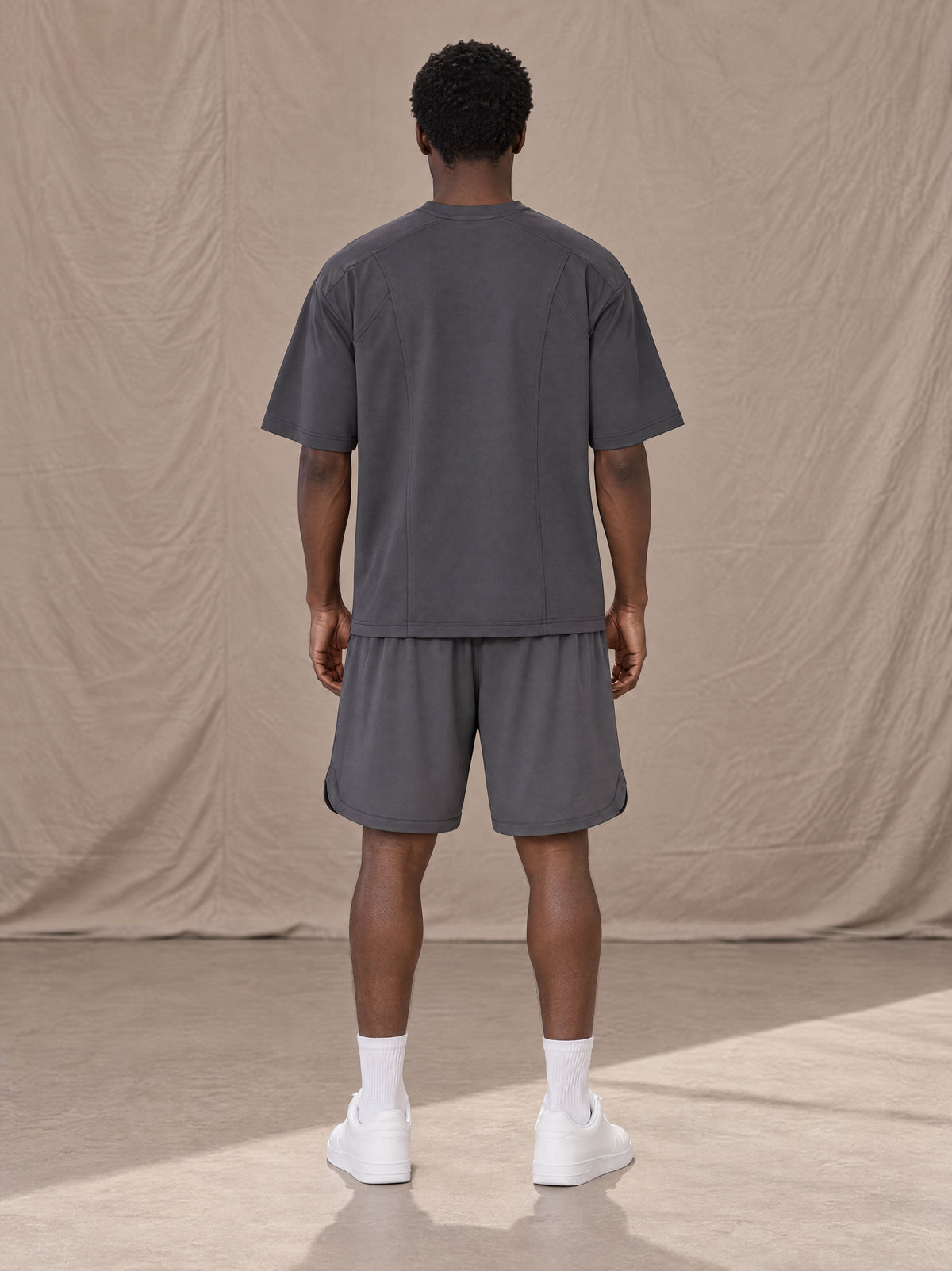Model wearing SM Motion T-shirt in Deep Charcoal with SM Motion Oversized Court Shorts in Deep Charcoal, rear view.