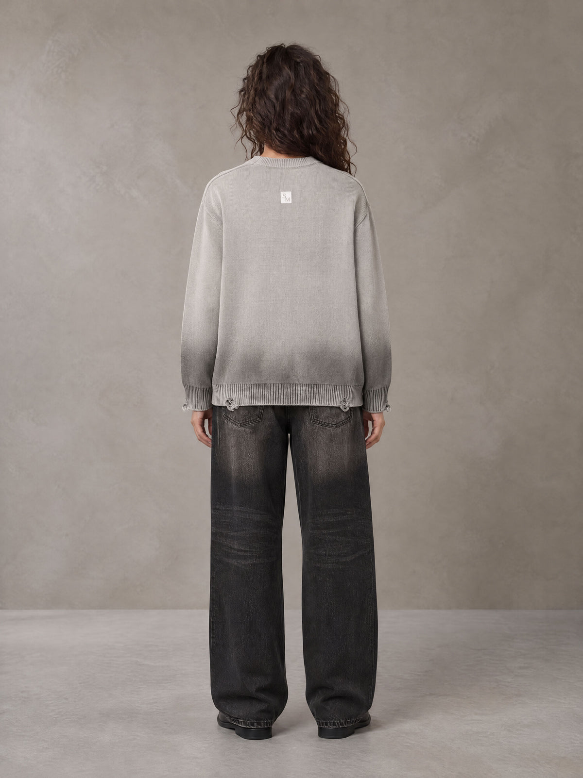 Model wearing the SM Sig. Washed Distress Knit Sweater in Warm Grey, rear view.
