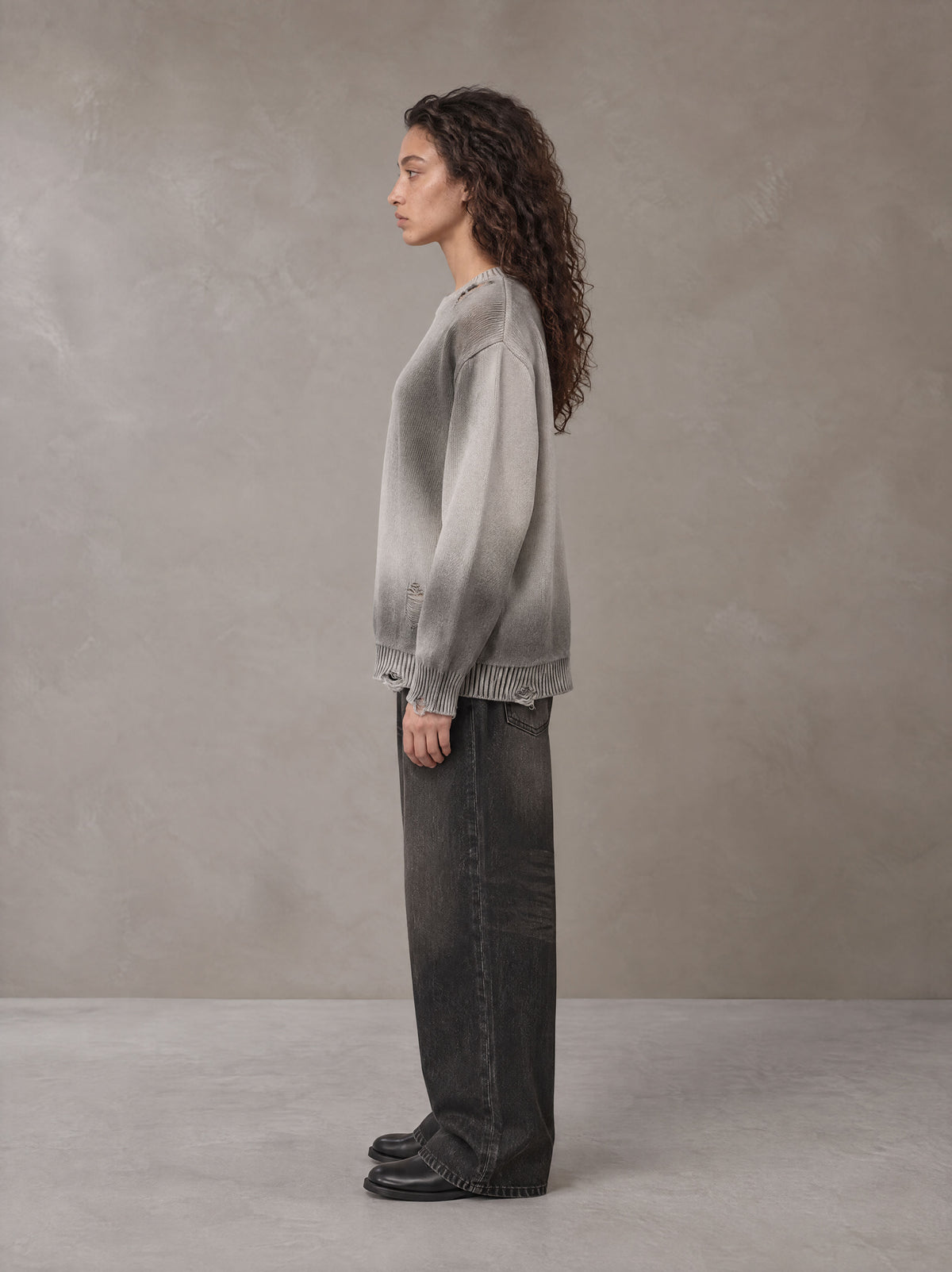Model wearing the SM Sig. Washed Distress Knit Sweater in Warm Grey, side profile.