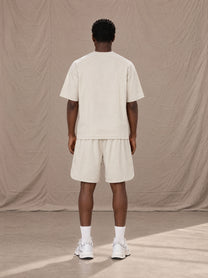 Model wearing SM Motion T-shirt in Oat Grey and SM Motion Oversized Court Shorts in Oat Grey, rear view.