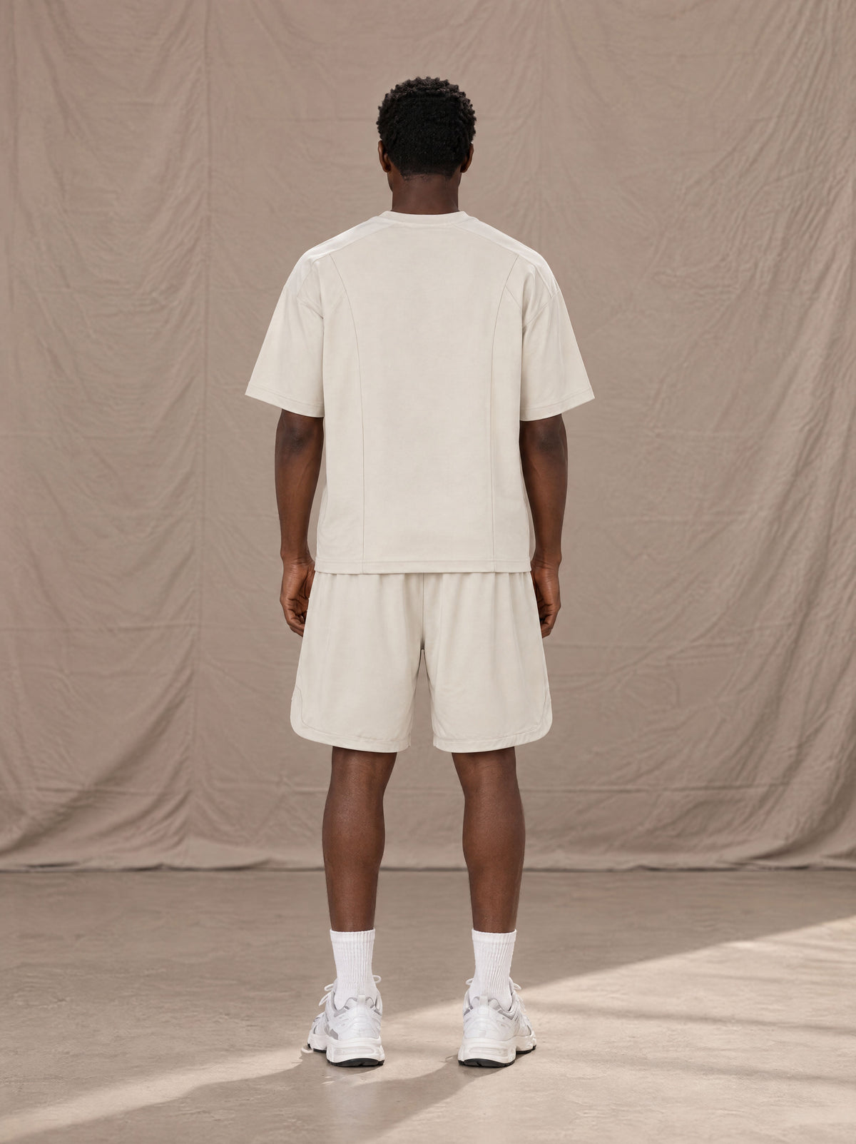 Model wearing SM Motion T-shirt in Oat Grey and SM Motion Oversized Court Shorts in Oat Grey, rear view.