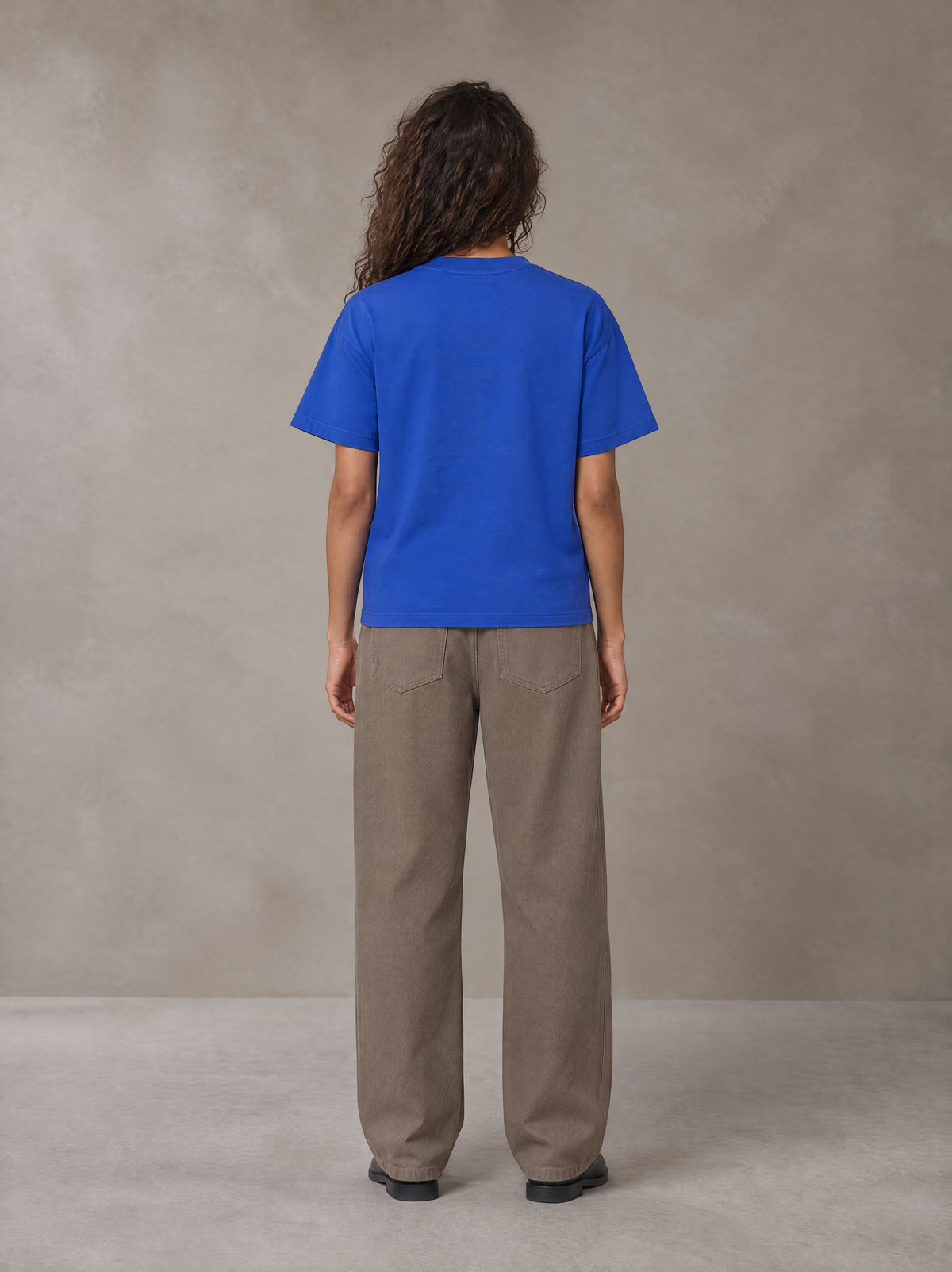 Model wearing SM Sig. Earth T-shirt in Classic Blue, rear view.
