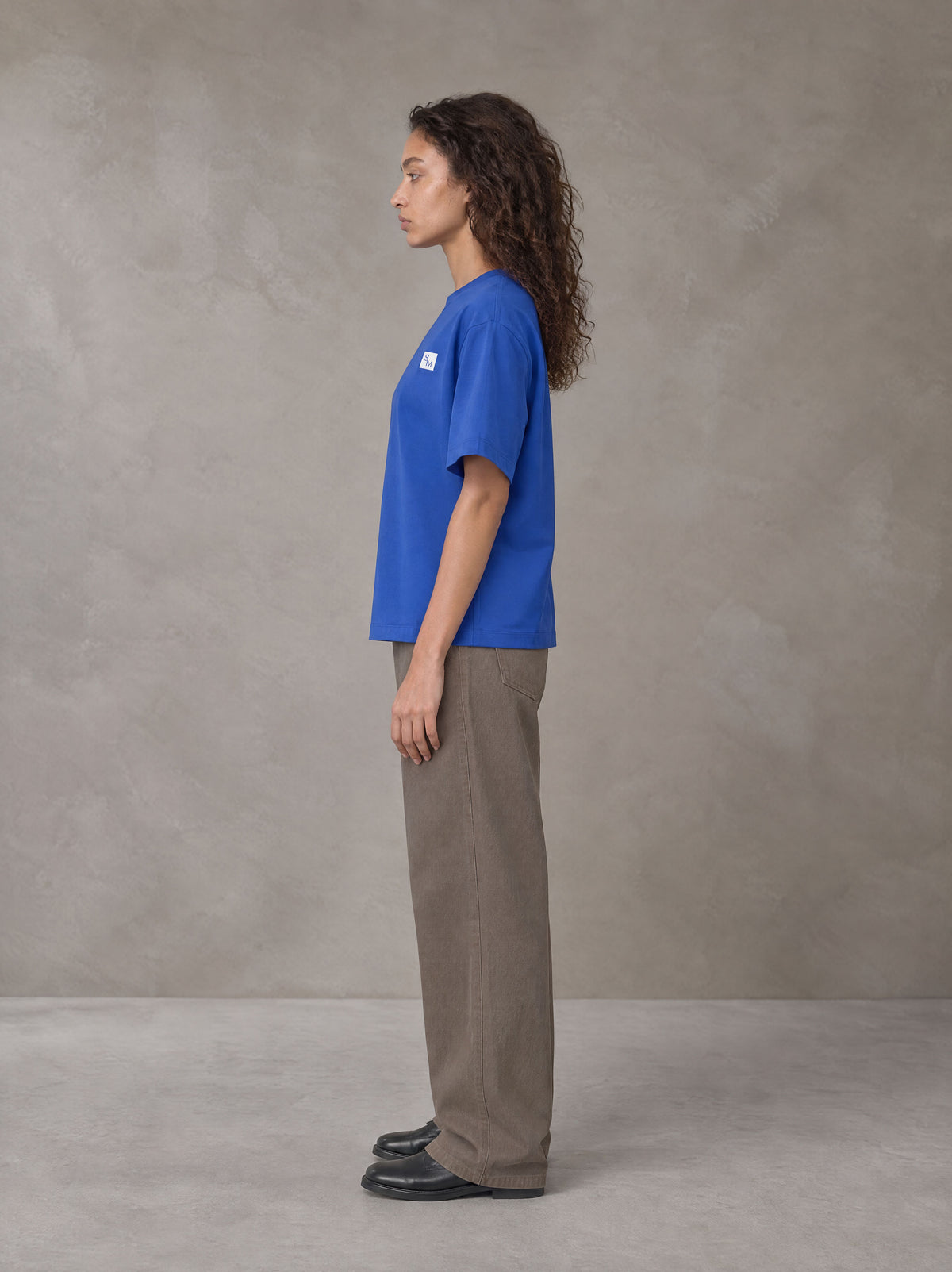 Model wearing SM Sig. Earth T-shirt in Classic Blue, side profile.