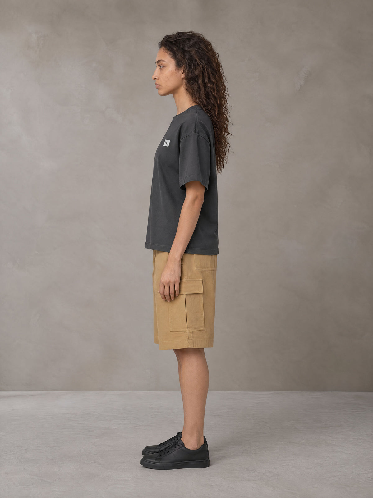 Model wearing SM Sig. Earth T-shirt in Deep Charcoal, side profile.