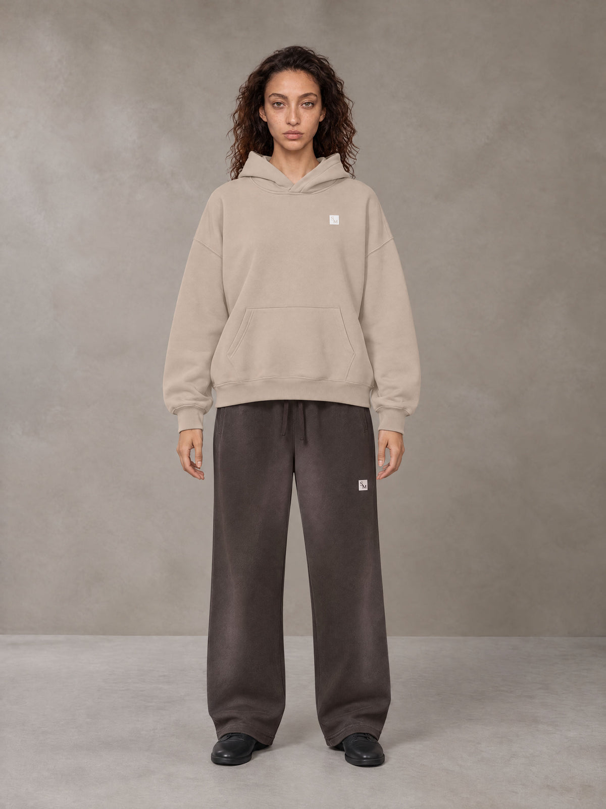 Model wearing SM Sig. Fleece Hoodie in Apricot Grey, front view.
