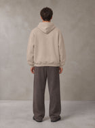 Model wearing SM Sig. Fleece Hoodie in Apricot Grey, rear view.