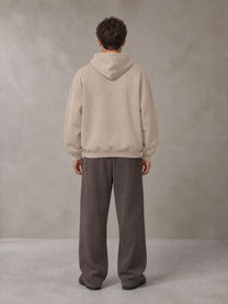 Model wearing SM Sig. Fleece Hoodie in Apricot Grey, rear view.