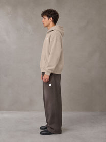Model wearing SM Sig. Fleece Hoodie in Apricot Grey, side profile.
