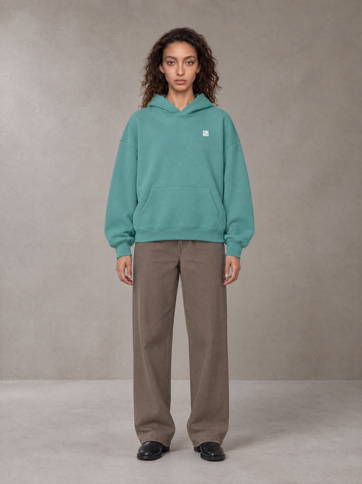 Model wearing SM Sig. Fleece Hoodie in Classic Green, front view.