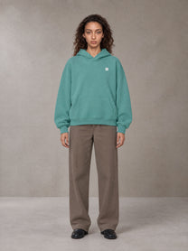 Model wearing SM Sig. Fleece Hoodie in Classic Green, front view.