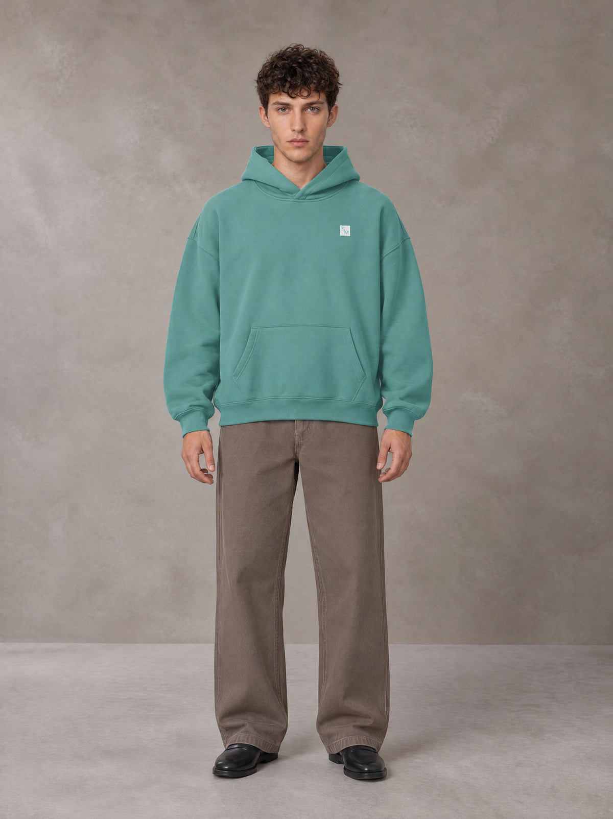 Model wearing SM Sig. Fleece Hoodie in Classic Green, front view.