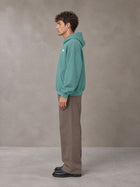 Model wearing SM Sig. Fleece Hoodie in Classic Green, side profile.