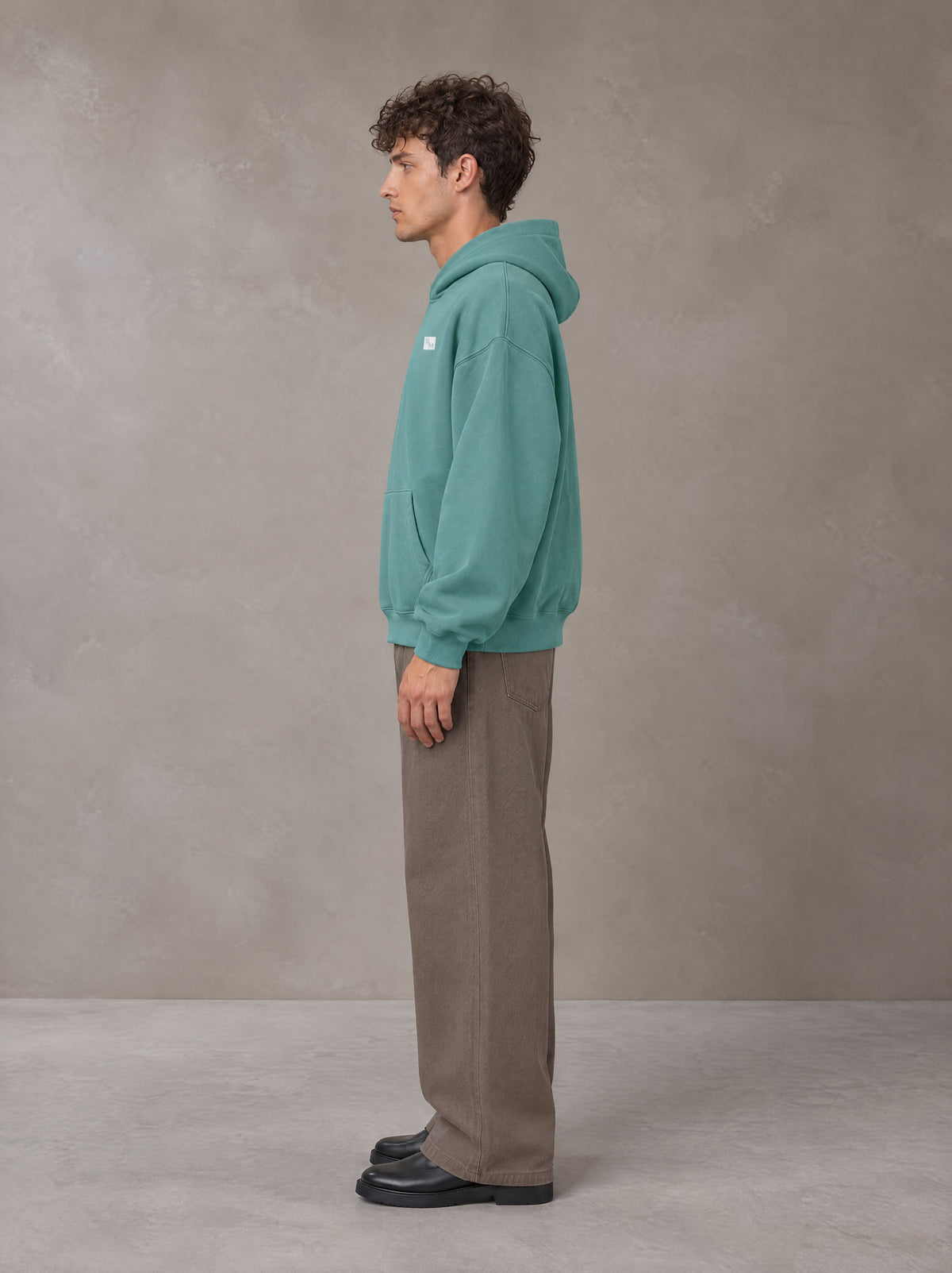 Model wearing SM Sig. Fleece Hoodie in Classic Green, side profile.