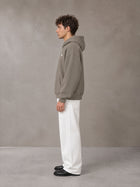 Model wearing SM Sig. Fleece Hoodie in Coffee Grey, side profile.