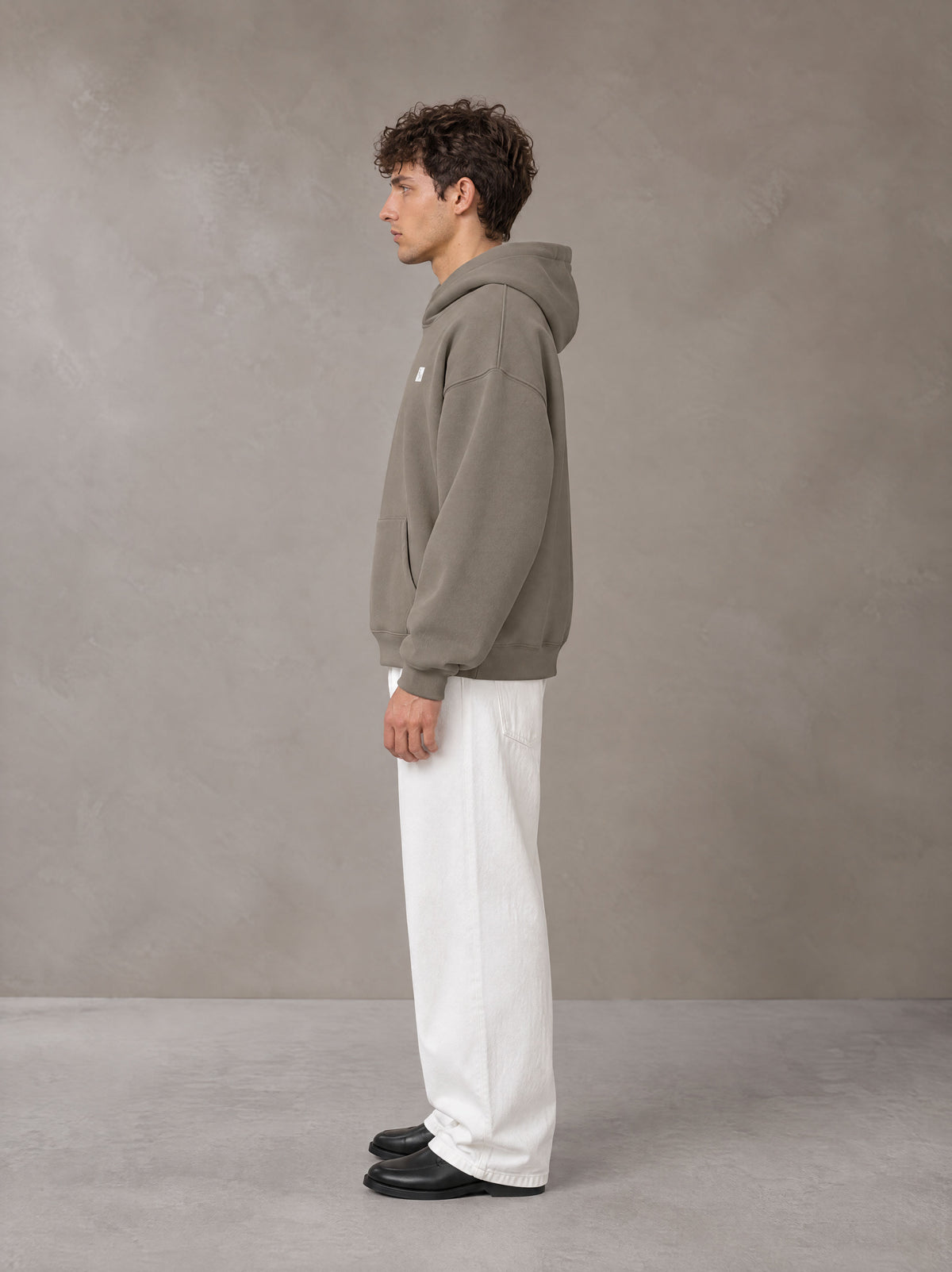 Model wearing SM Sig. Fleece Hoodie in Coffee Grey, side profile.