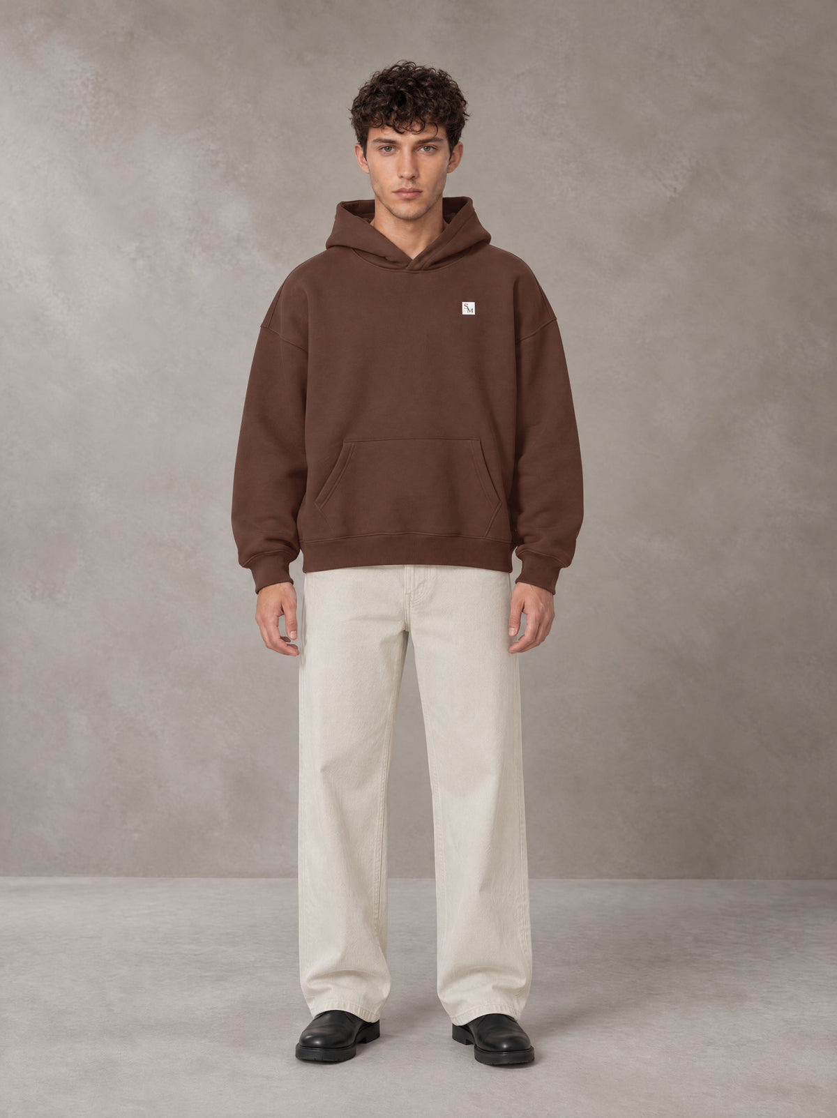 Model wearing SM Sig. Fleece Hoodie in Deep Coffee, front view.