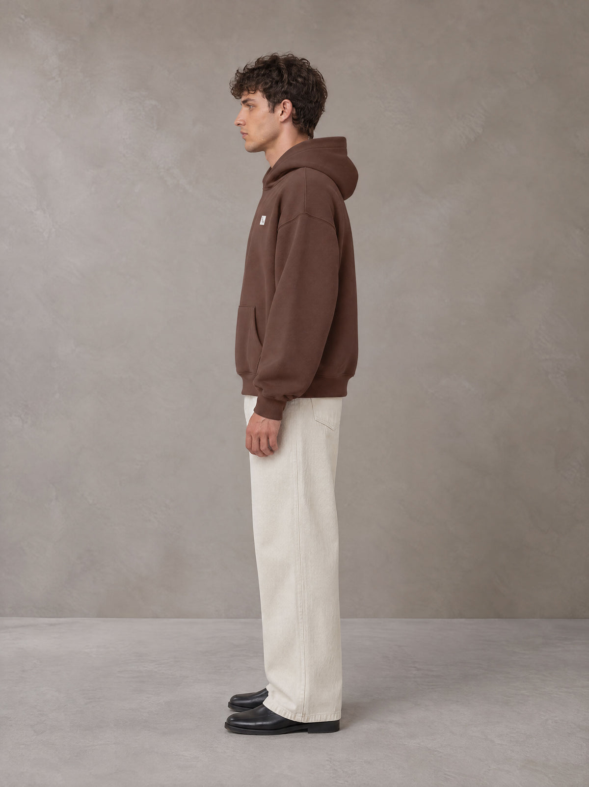 Model wearing SM Sig. Fleece Hoodie in Deep Coffee, side profile.