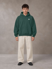 Model wearing SM Sig. Fleece Hoodie in Eden Green, front view.