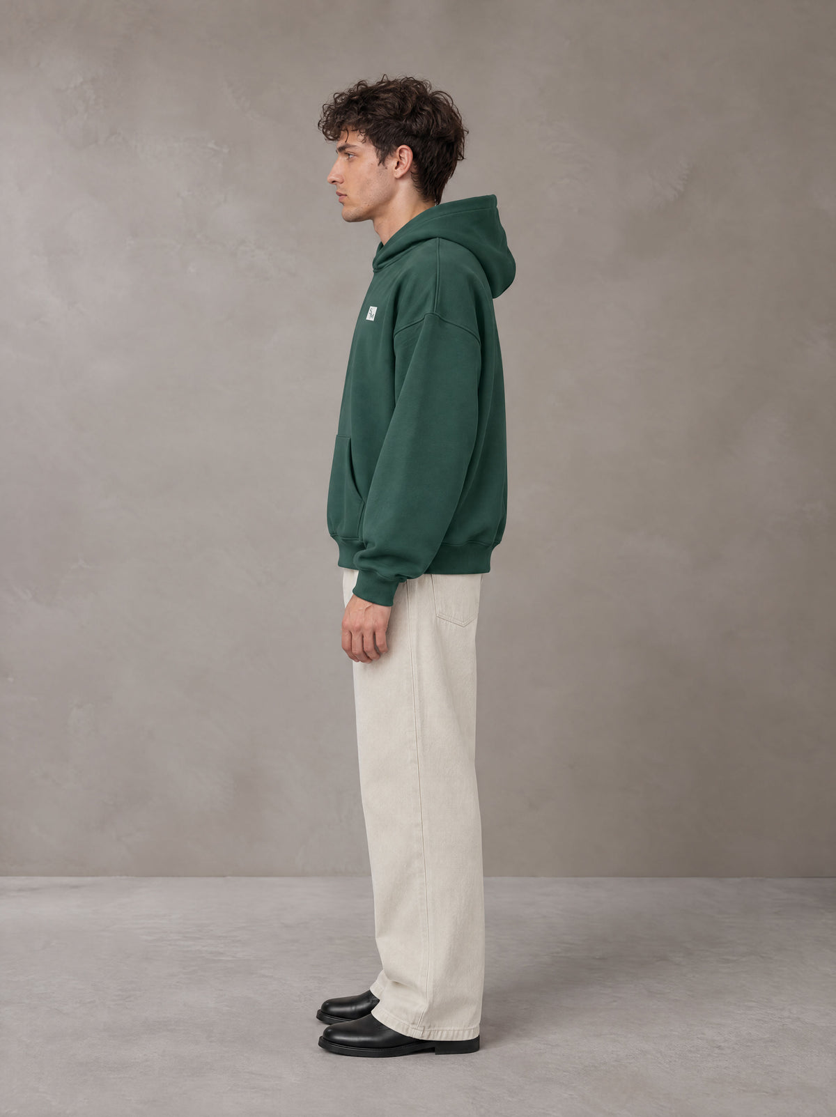 Model wearing SM Sig. Fleece Hoodie in Eden Green, side profile.