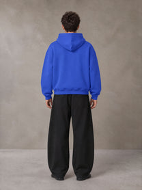 Model wearing SM Sig. Fleece Hoodie in Klein Blue, rear view.