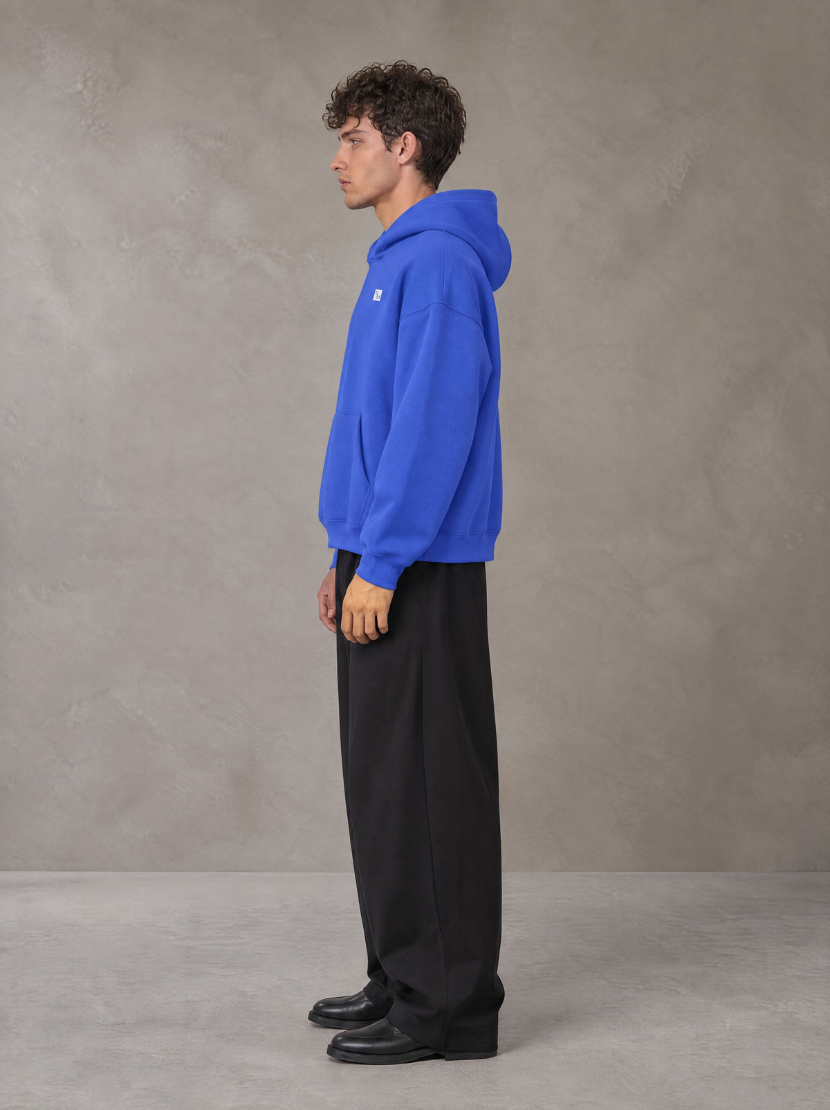 Model wearing SM Sig. Fleece Hoodie in Klein Blue, side profile.
