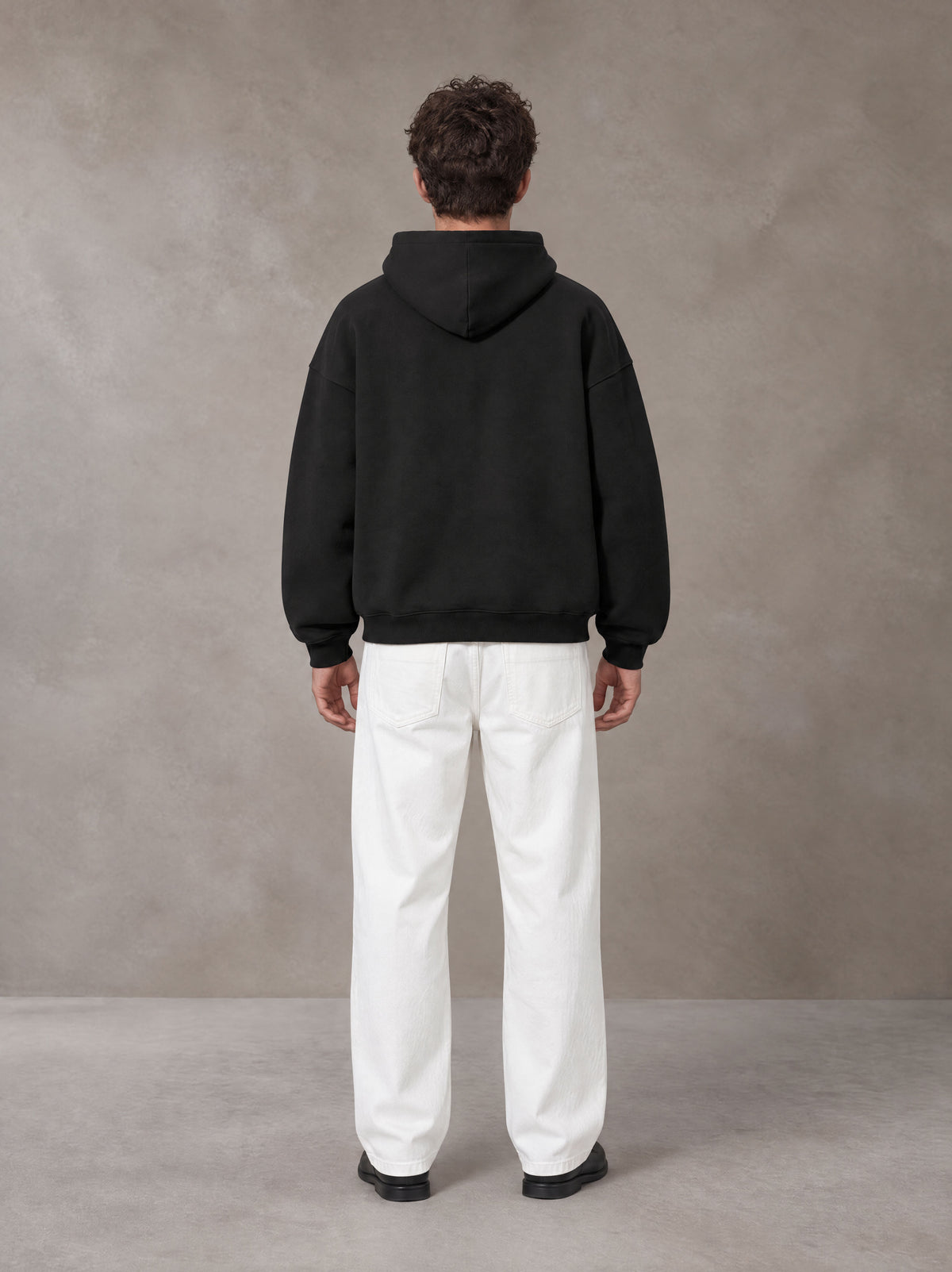 Model wearing SM Sig. Fleece Hoodie in Midnight Black, rear view.