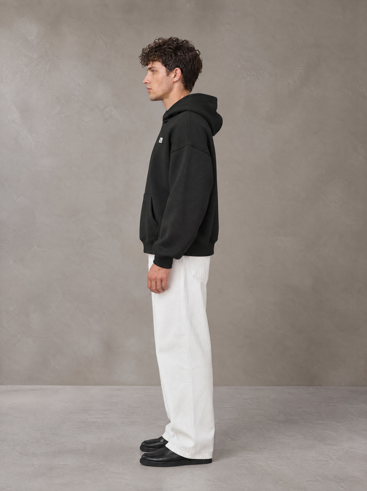Model wearing SM Sig. Fleece Hoodie in Midnight Black, side profile.