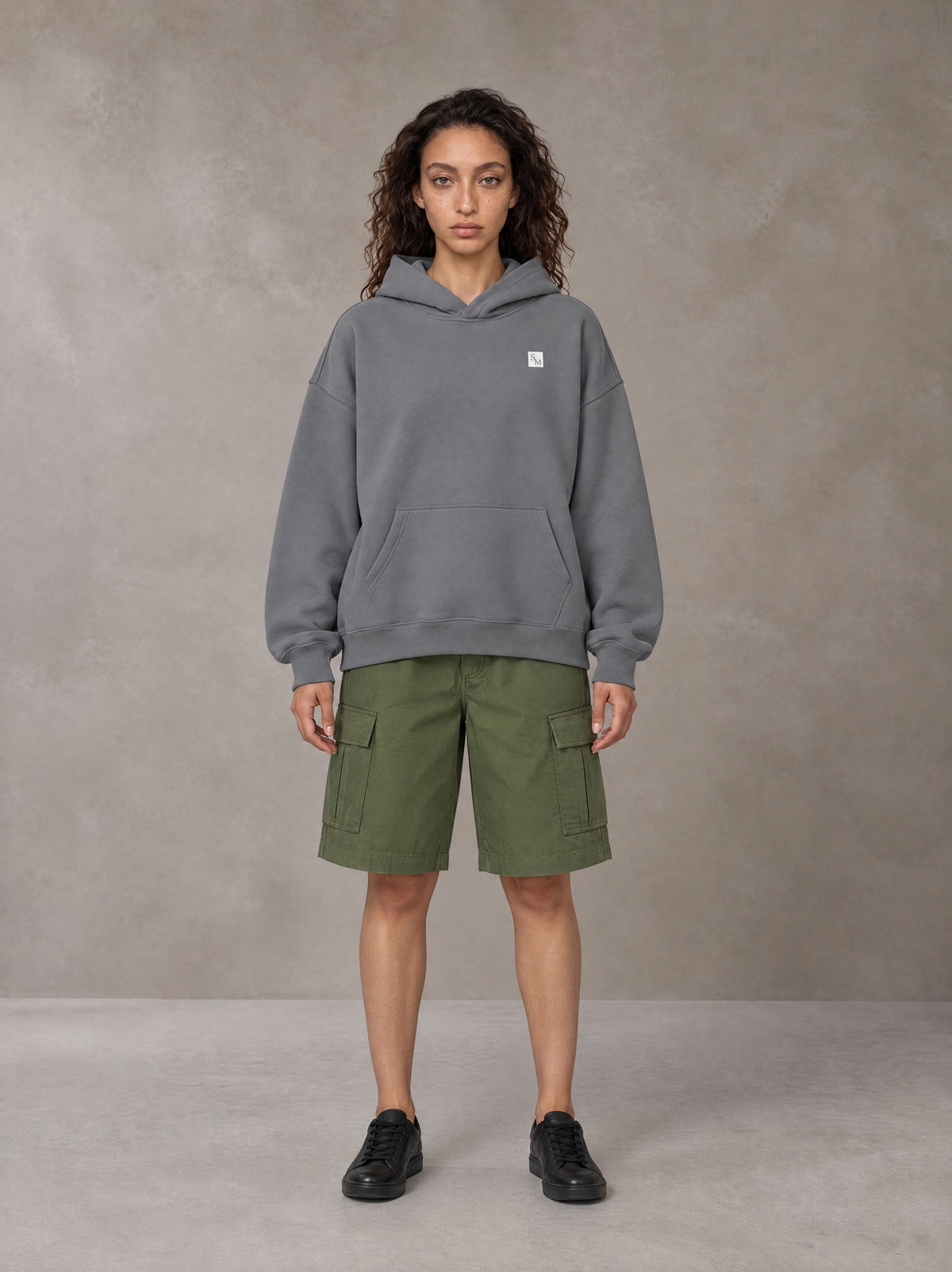 Model wearing SM Sig. Fleece Hoodie in Pure Grey, front view.