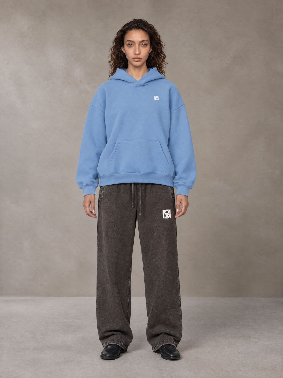 Model wearing SM Sig. Fleece Hoodie in Soft Blue, front view.