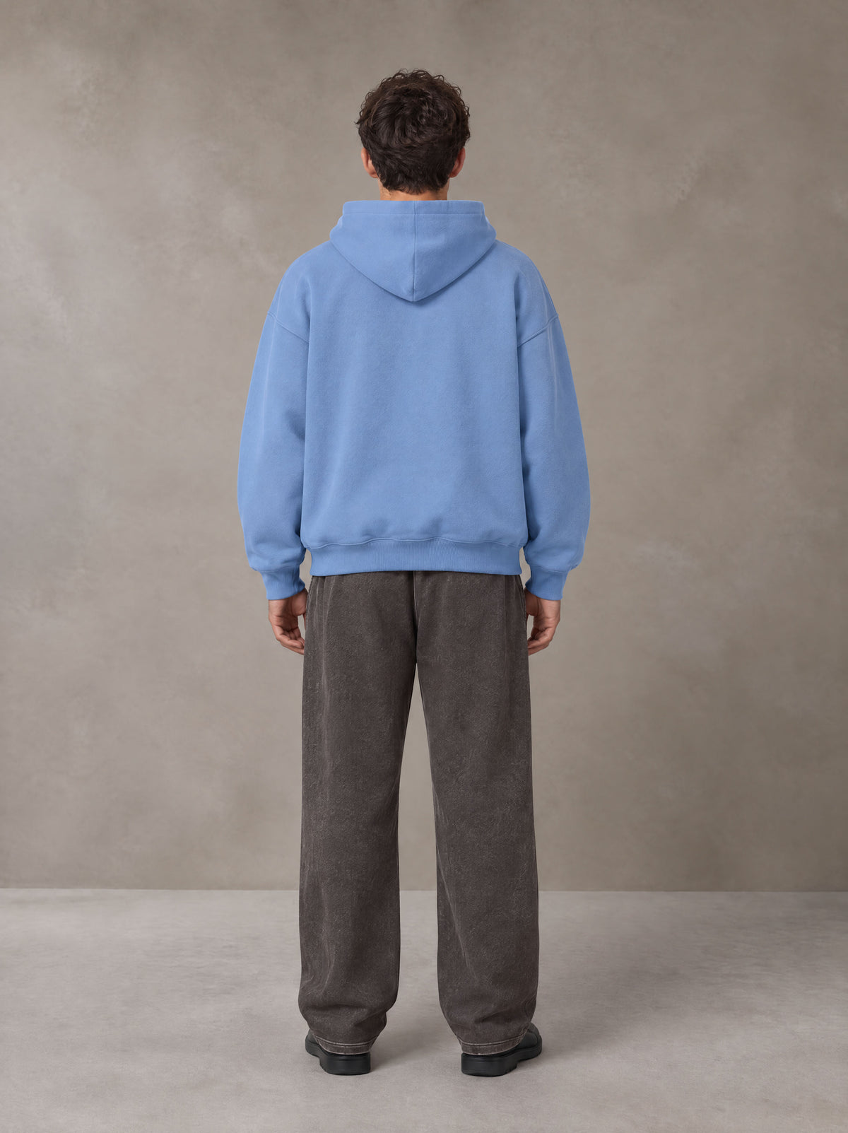 Model wearing SM Sig. Fleece Hoodie in Soft Blue, rear view.